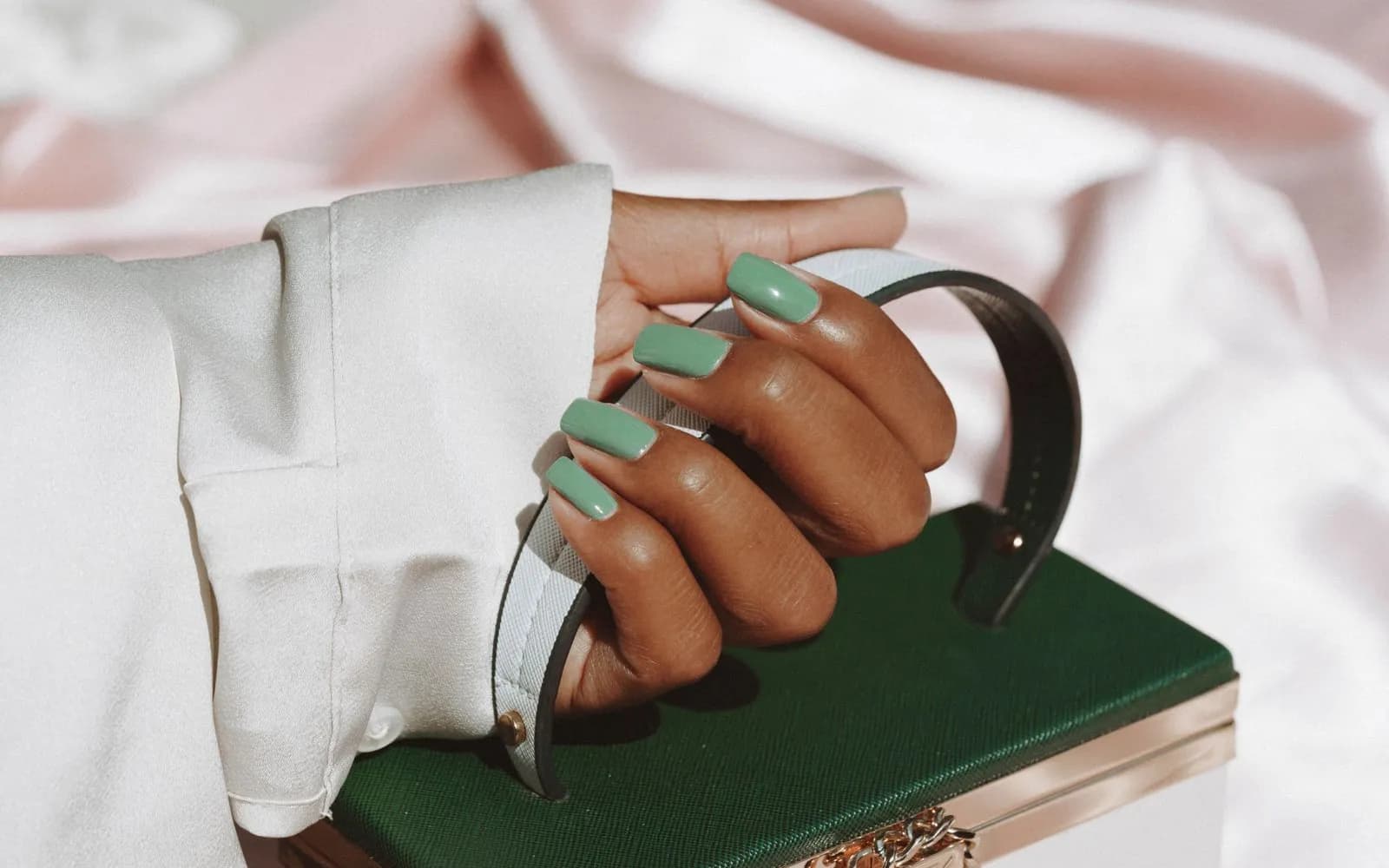 A hand with green gel polish holding an elegant bag