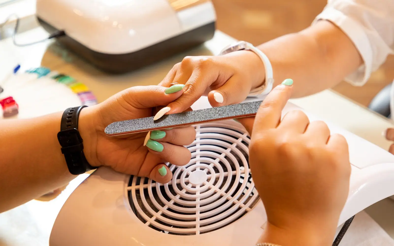 Lixando as unhas verde-menta de uma cliente em uma mesa de manicure