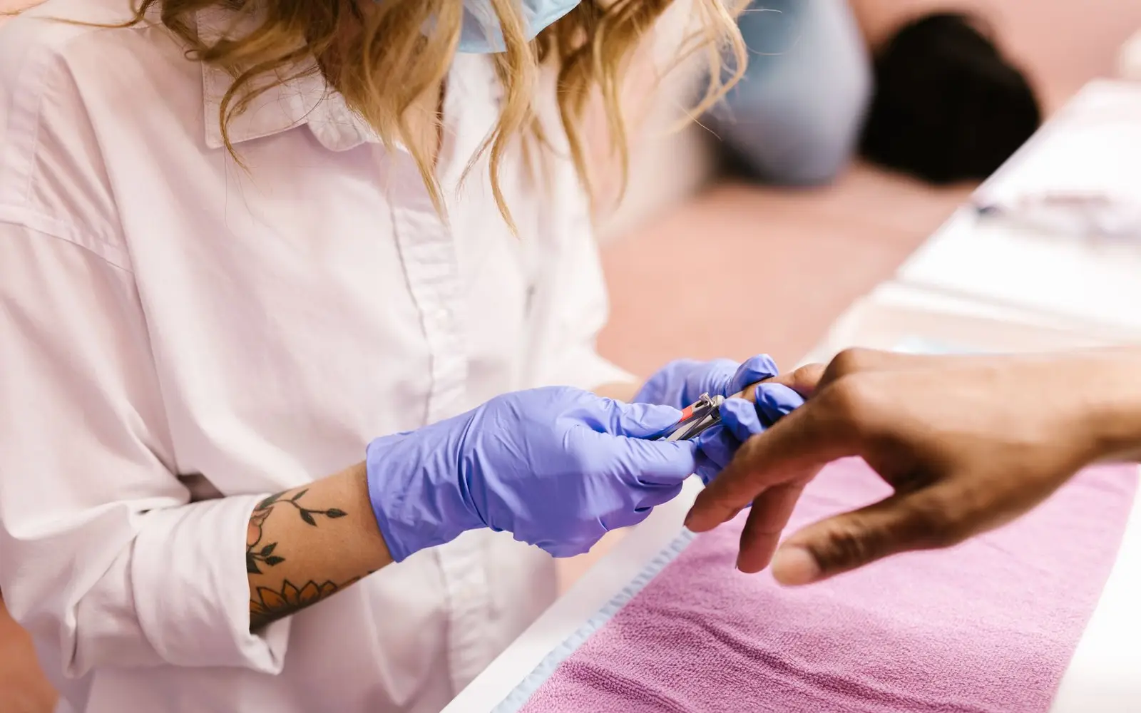 A nail technician trimming a client's nails at the manicure table