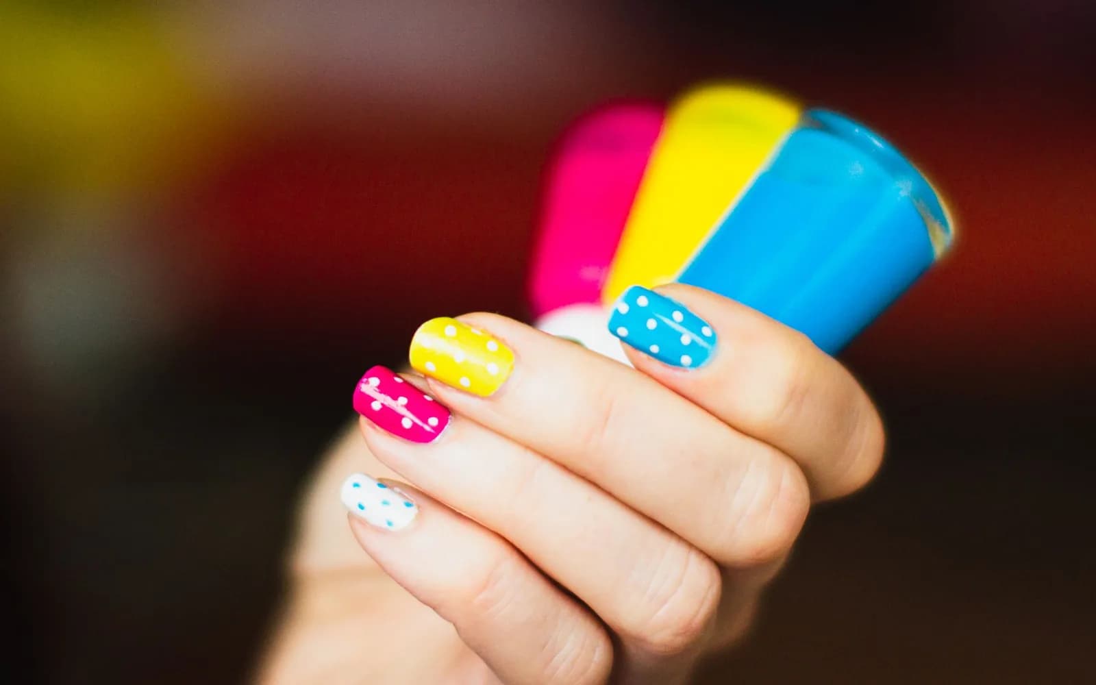 Colorful polka dot nail art on a hand holding nail polish bottles