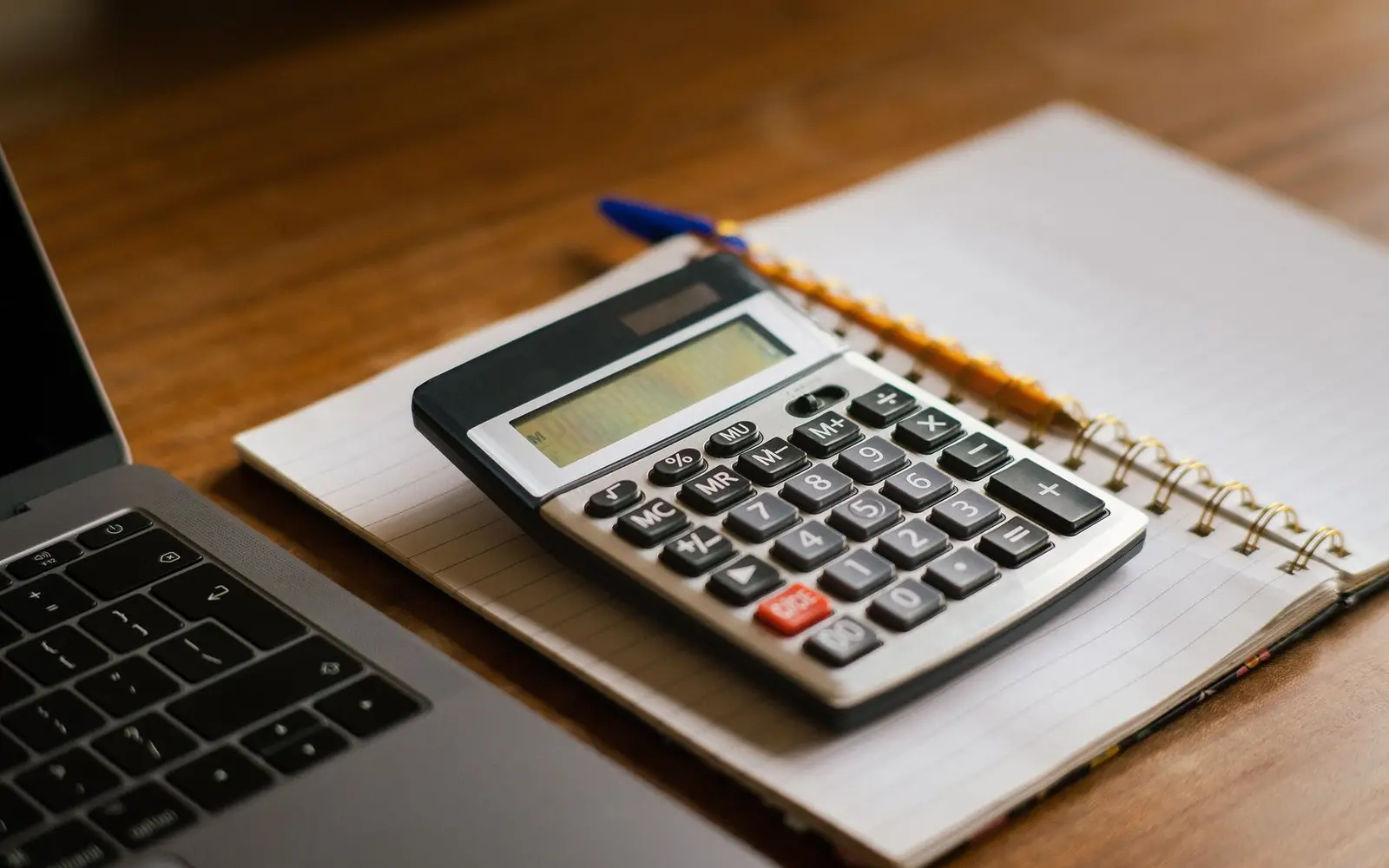 Une calculatrice et un carnet à côté d'un ordinateur portable